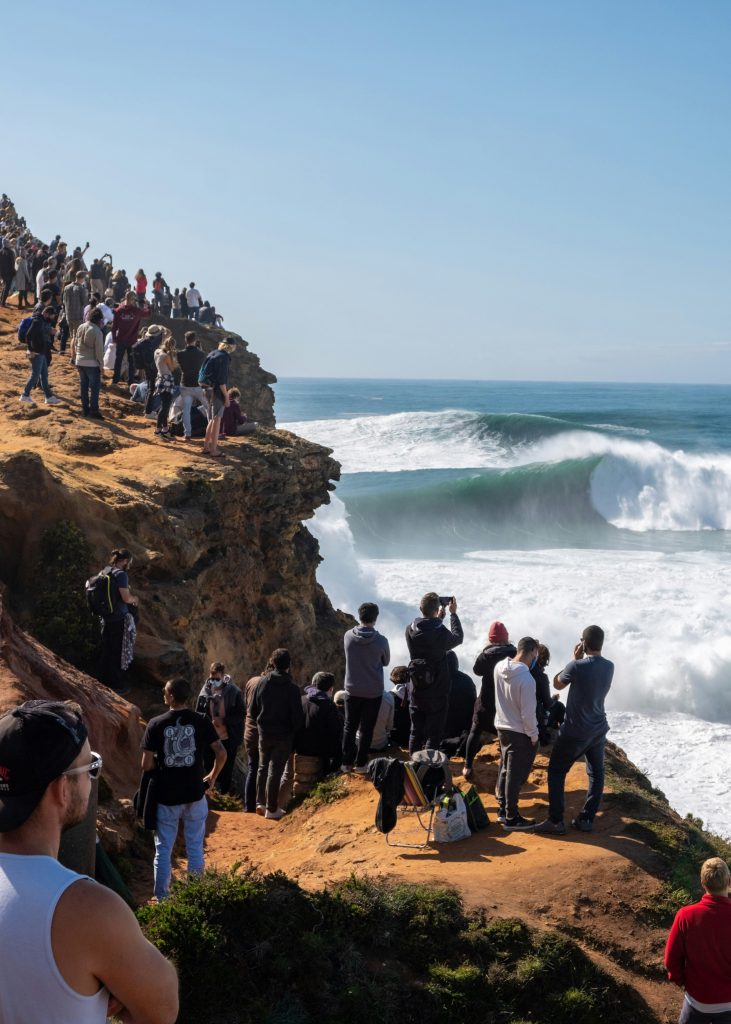 Nazaré giant Atlantic waves with surfers and cliffside lighthouse overlooking the ocean