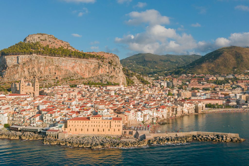 Cefalù medieval coastal town with stone houses, historic cathedral, narrow streets, and a sandy beach set against the blue Mediterranean Sea