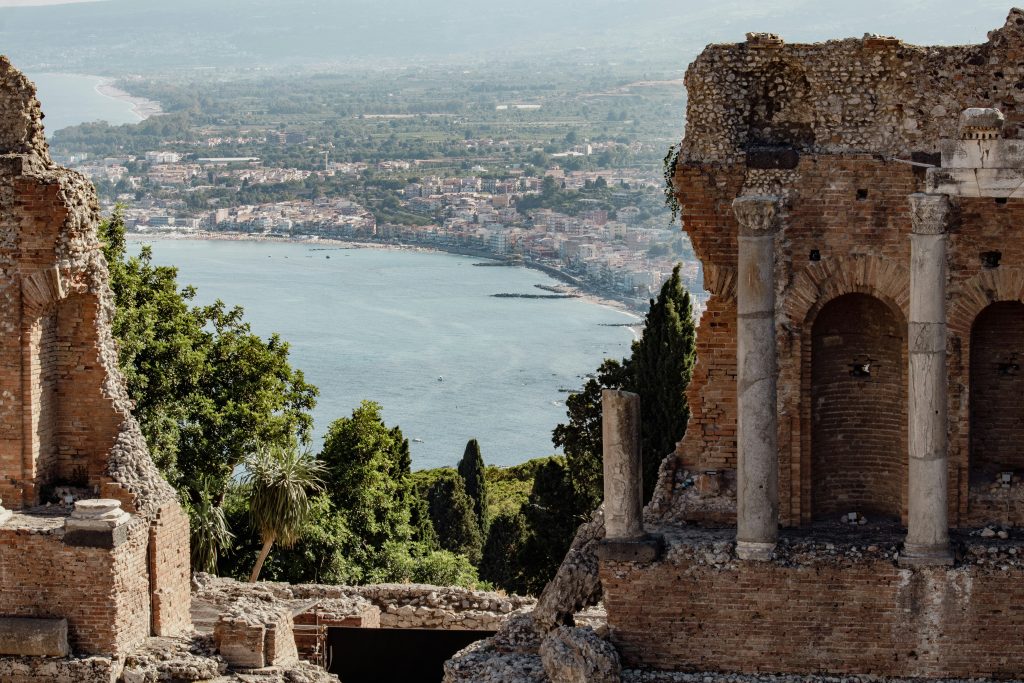 East Coast of Sicily showing Mount Etna towering above Catania and Taormina, with volcanic coastline, baroque architecture, seaside cliffs, and contrasting urban energy and elegant hilltop scenery