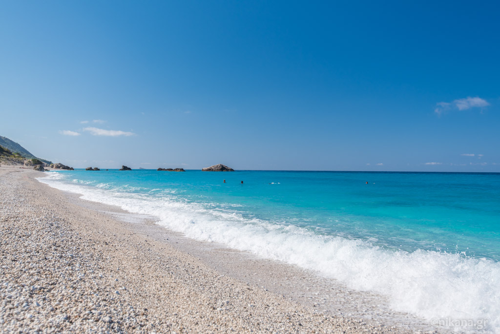 Kathisma Beach Lefkada with golden sand, organized sunbeds, beach bars and turquoise sea at sunset.