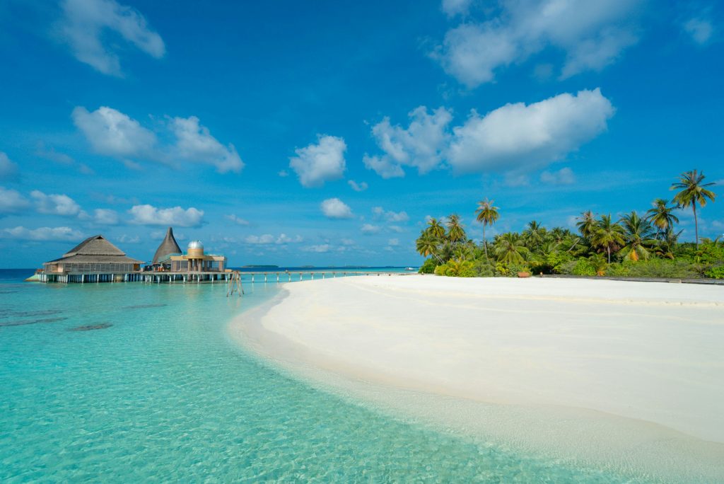 Maldives beach with white sand, crystal-clear turquoise water, and tropical palm trees