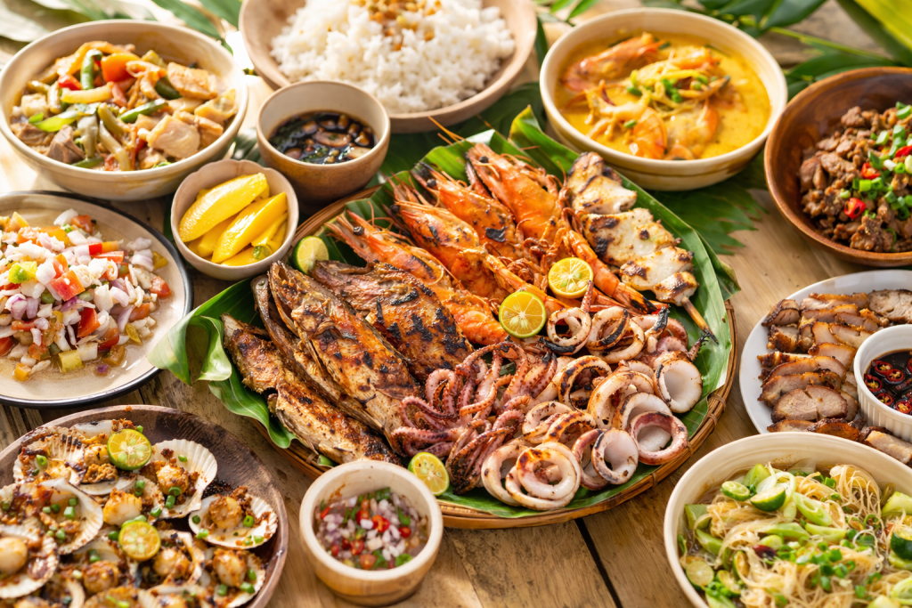 tropical food spread with seafood, grilled meats, and filipino dishes in a beach setting