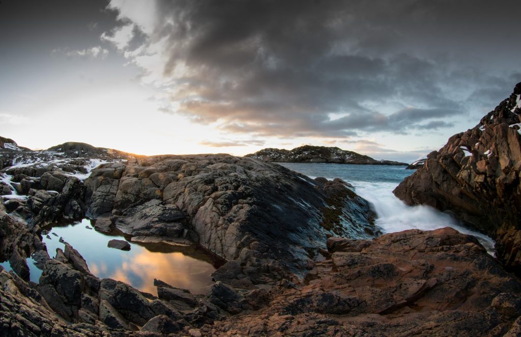 Rocky coastline with waves, dramatic clouds, and sunset light reflecting on water