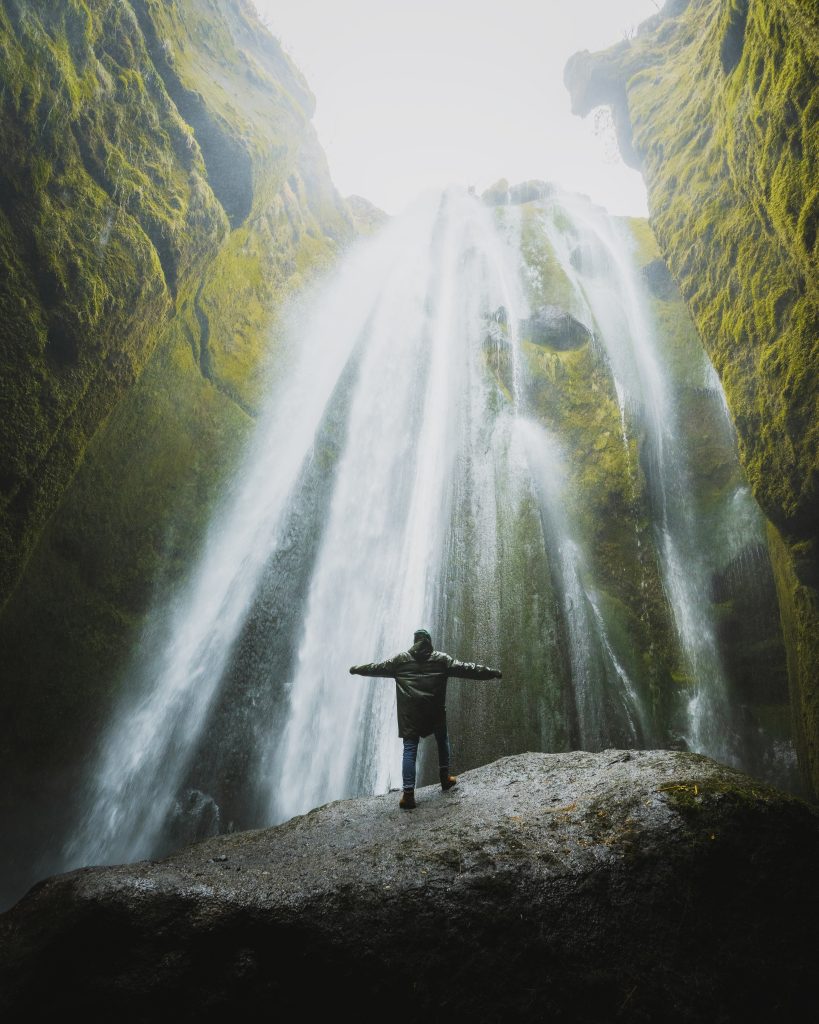 Waterfall in Iceland with person standing in front of powerful cascade – Iceland travel guide