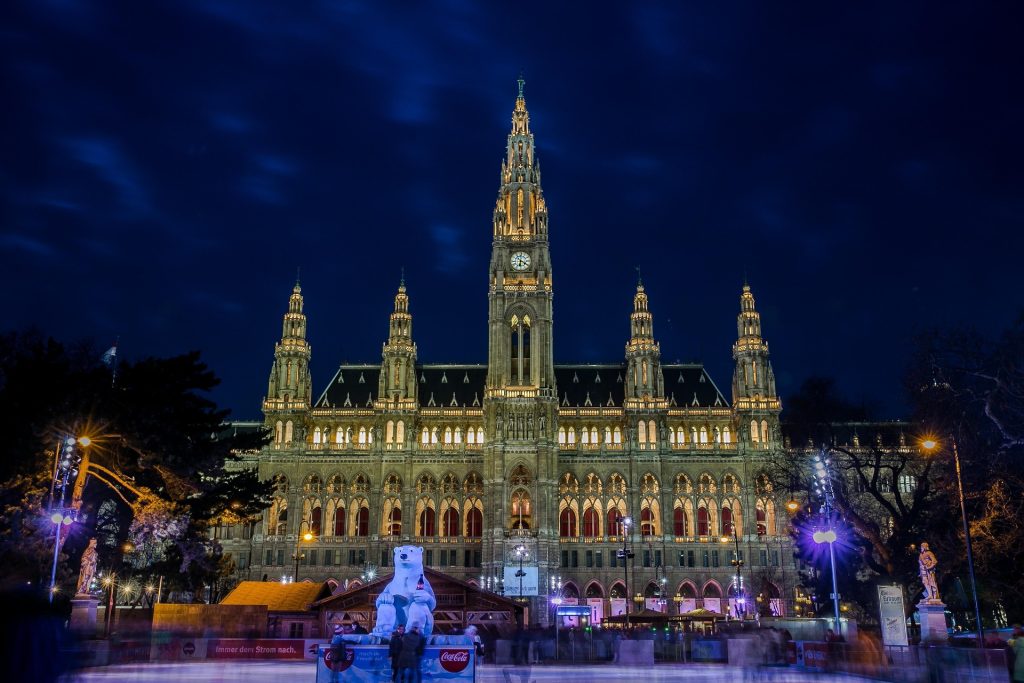 Vienna city hall illuminated at night with lights and people in the square
