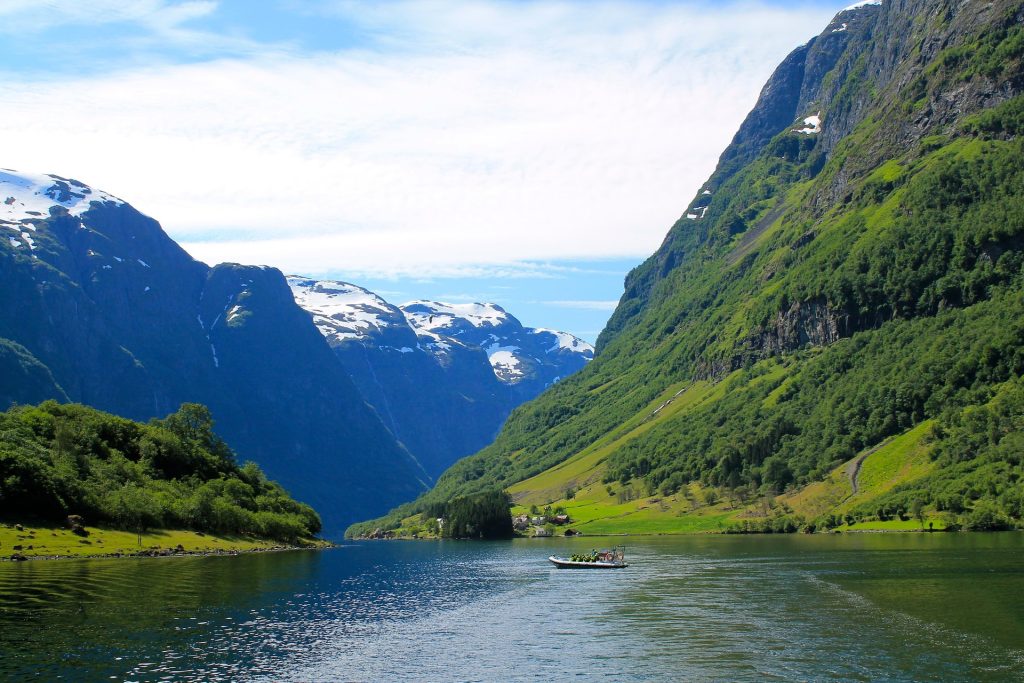 Green fjord landscape with steep mountains, calm water, and small boat in Norway