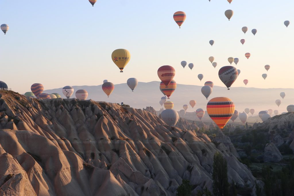 Hot air balloons flying over Cappadocia valleys during sunrise with soft light