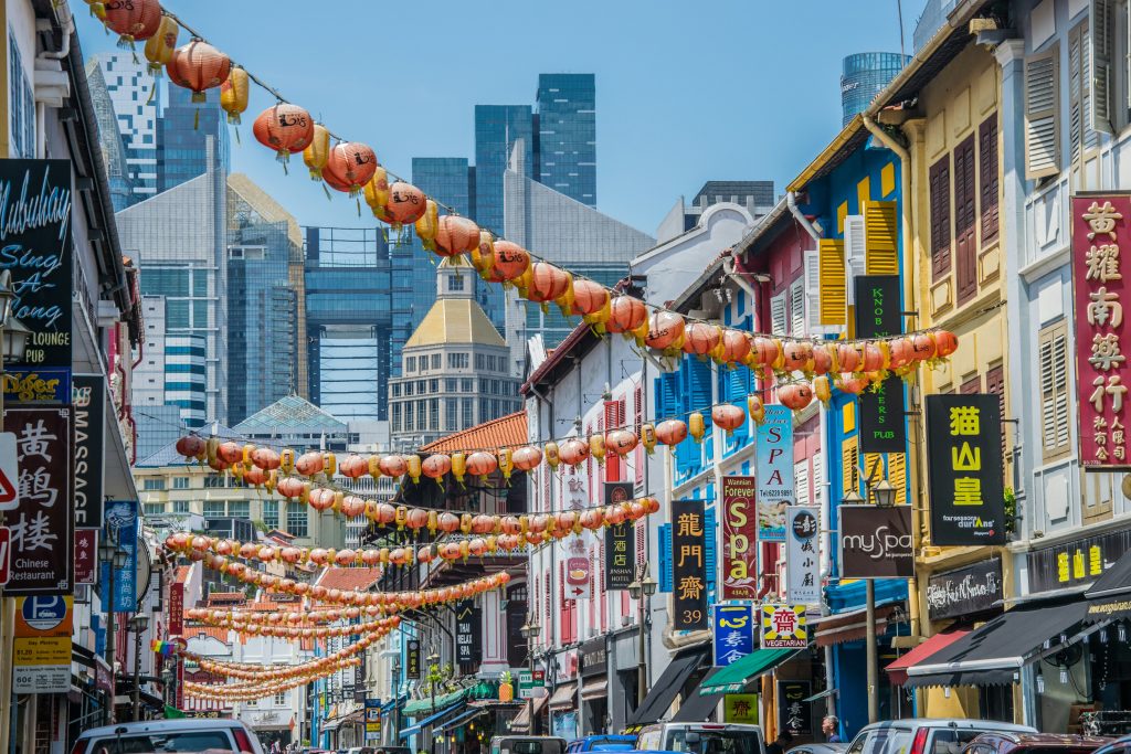 Colorful Chinatown street lined with lanterns, shophouses, and city skyscrapers in the distance