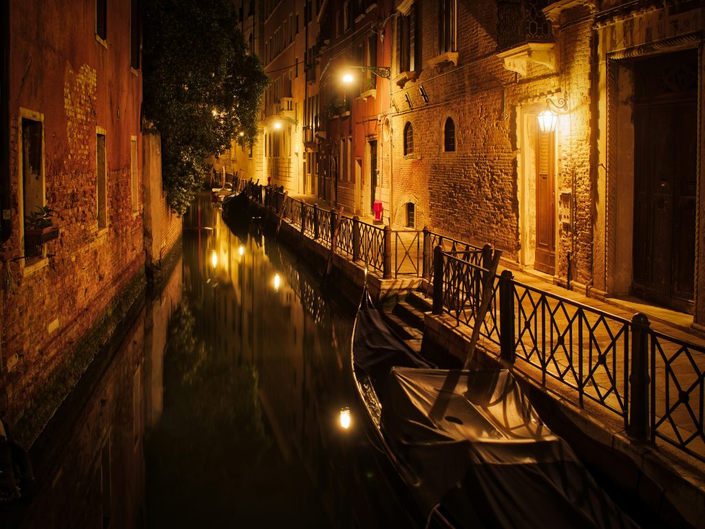 Venice canal at night with gondolas, glowing street lamps, and historic buildings reflected in the water