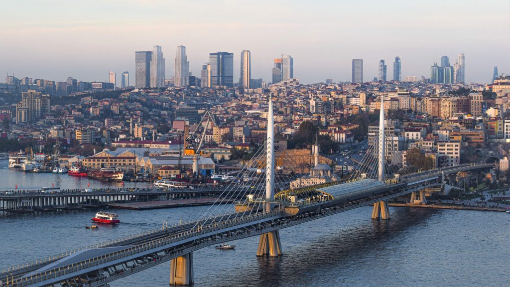 Modern bridge stretching across the Golden Horn with ferries, waterfront views, and the dense skyline of Istanbul in the background.