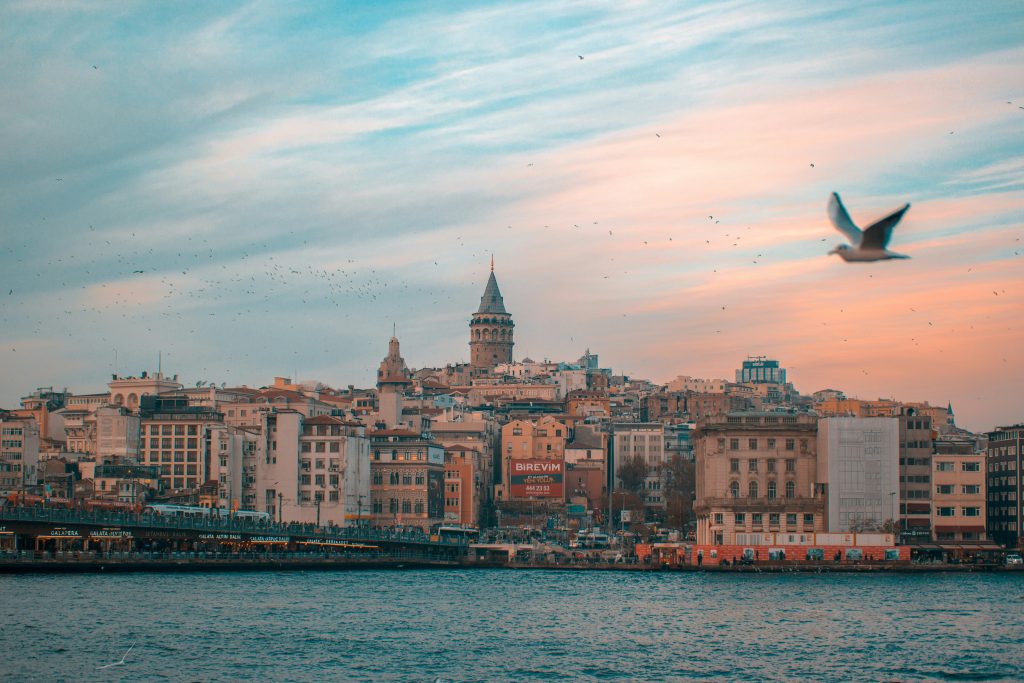 Soft pastel view of Istanbul skyline with Galata Tower rising above the city and calm Bosphorus waters in the foreground.