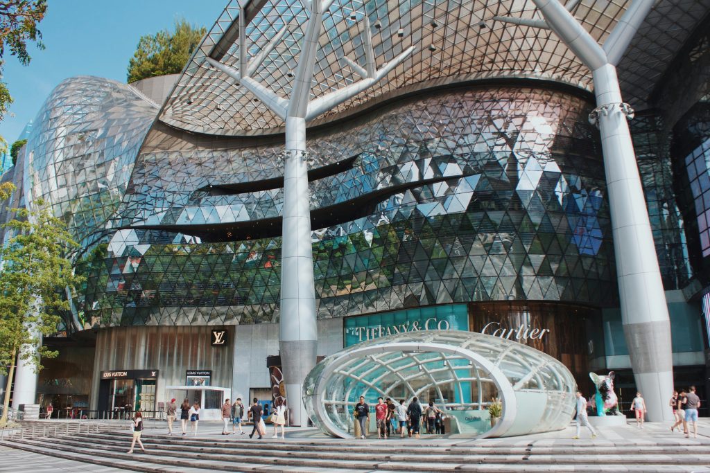 Futuristic shopping mall facade with glass architecture, luxury storefronts, and modern city design in Singapore