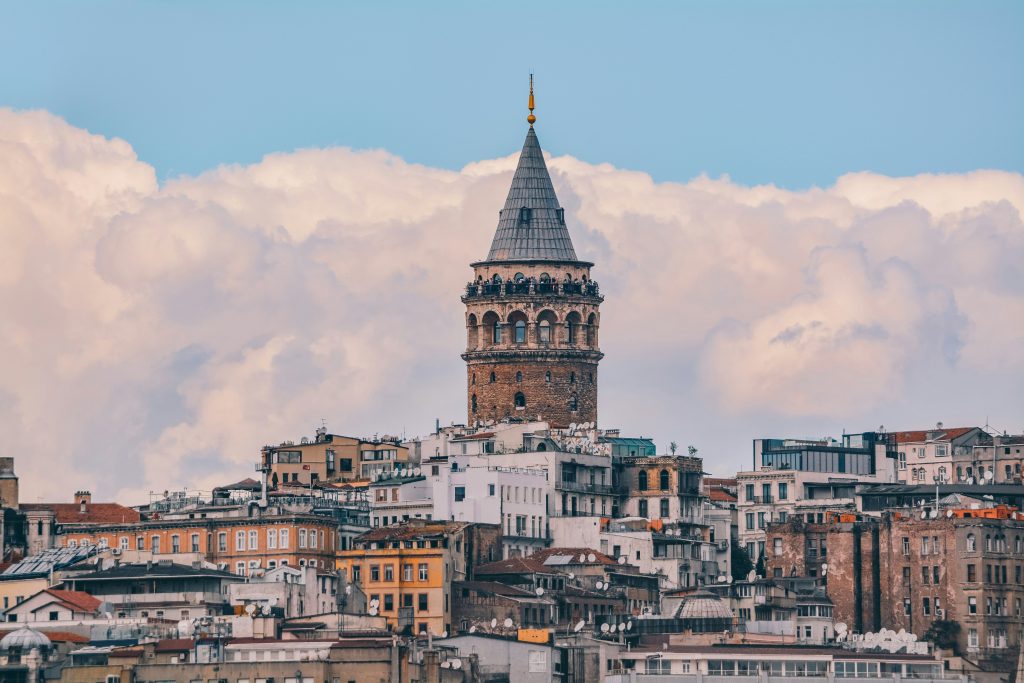 Close-up view of Galata Tower rising above historic Istanbul buildings under dramatic clouds and soft daylight.