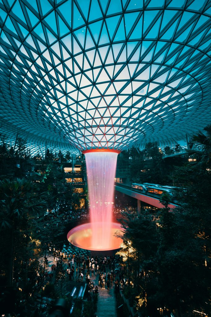 Interior view of Jewel Changi Airport with the Rain Vortex waterfall cascading beneath a glass dome surrounded by tropical greenery