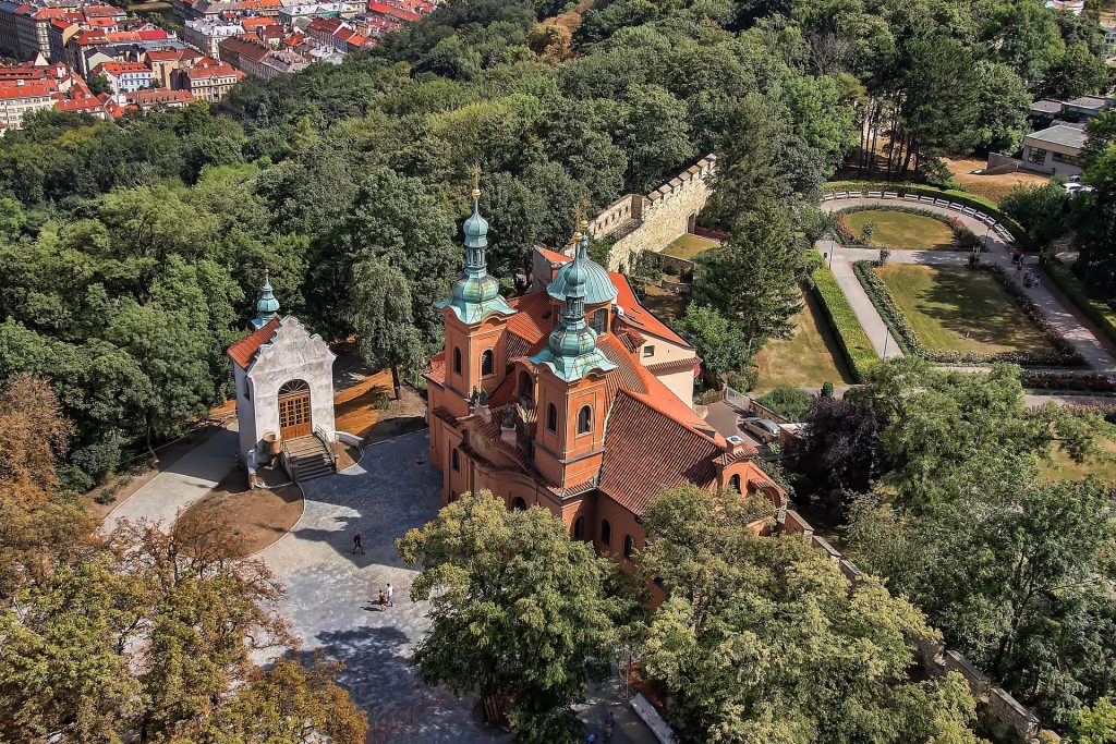 Aerial view of a peaceful church surrounded by trees, gardens, walking paths, and greenery above the city.