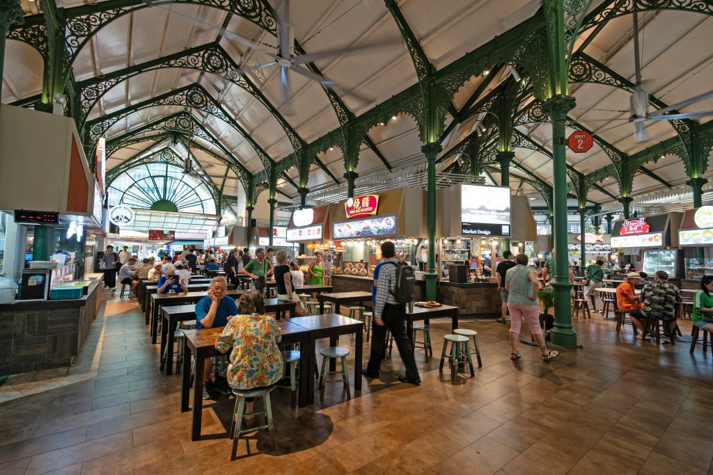 Busy hawker centre interior with food stalls, dining tables, and local atmosphere