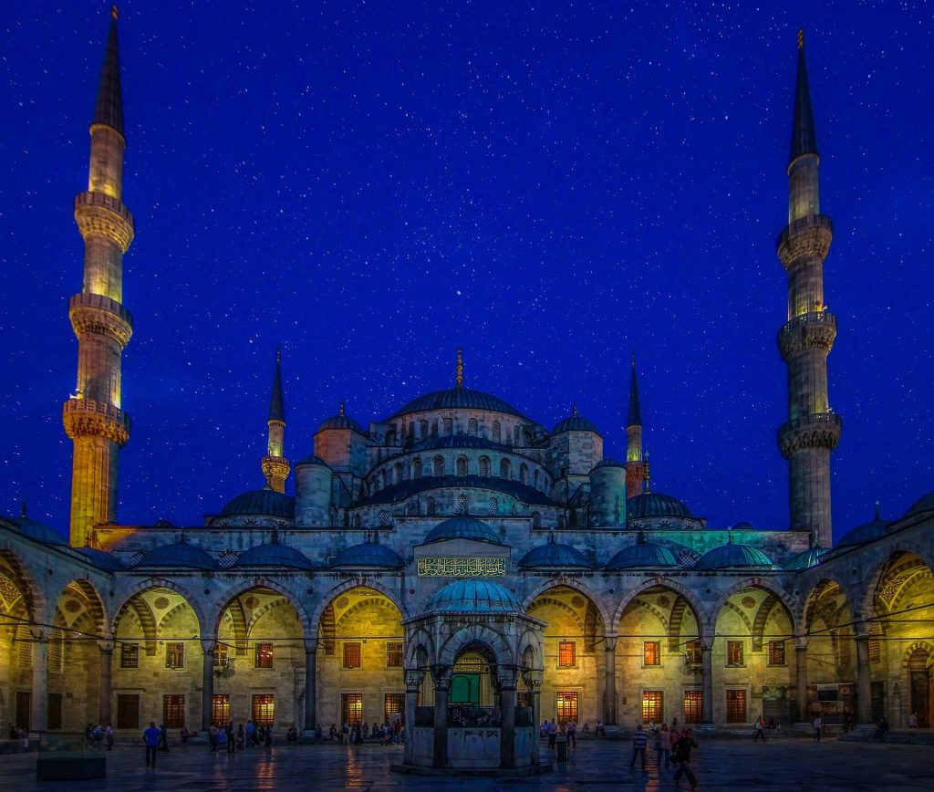 Blue Mosque illuminated at night with glowing arches, towering minarets, and a deep blue evening sky above Istanbul.