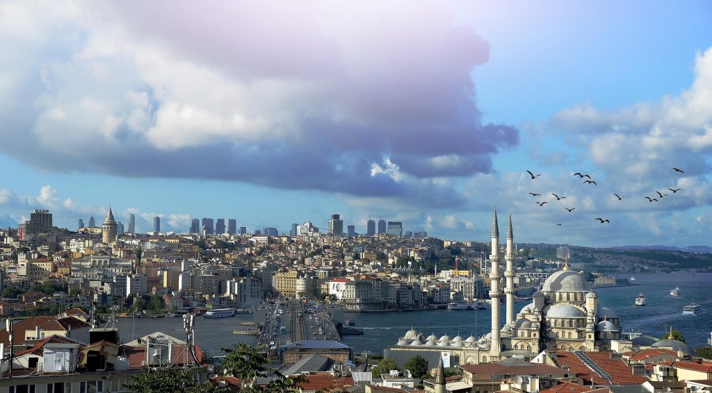 Panoramic view of Istanbul skyline with Galata Tower, historic mosques, dramatic clouds, and the Bosphorus stretching through the city.