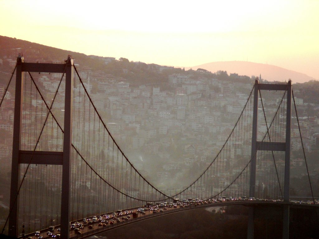 Sunlight glowing over the Bosphorus Bridge with heavy traffic crossing between the hills and skyline of Istanbul.