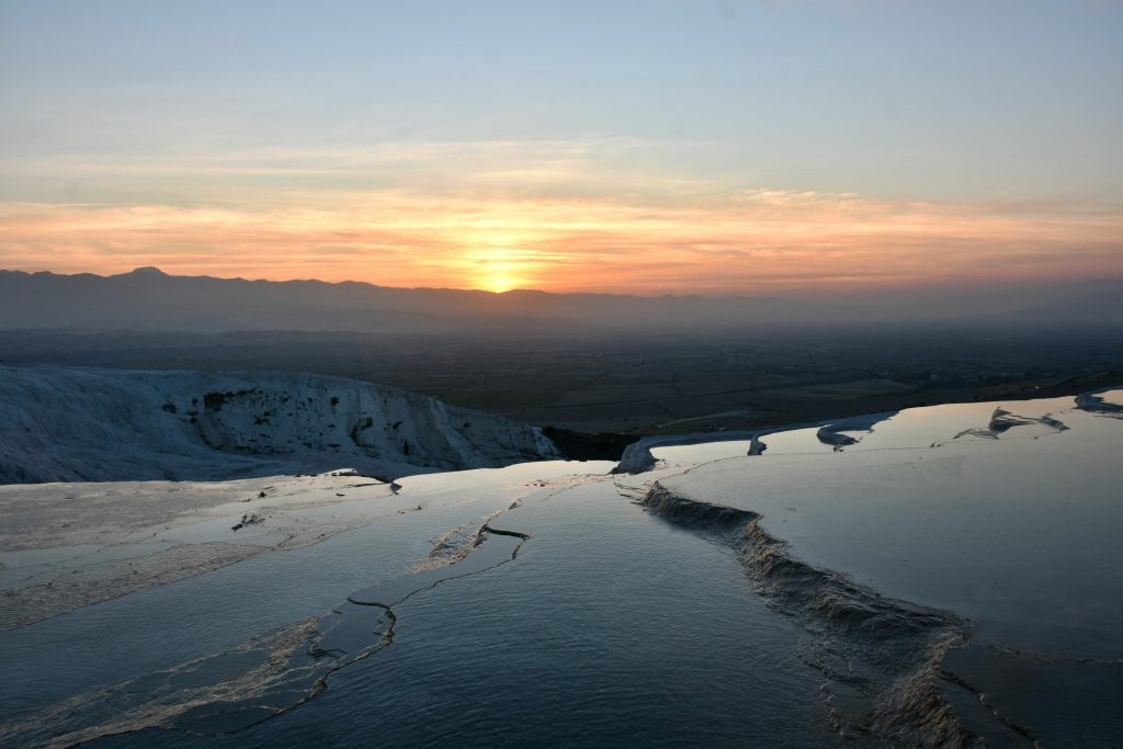 Panoramic sunset view over the white mineral terraces and thermal waters with distant mountain silhouettes