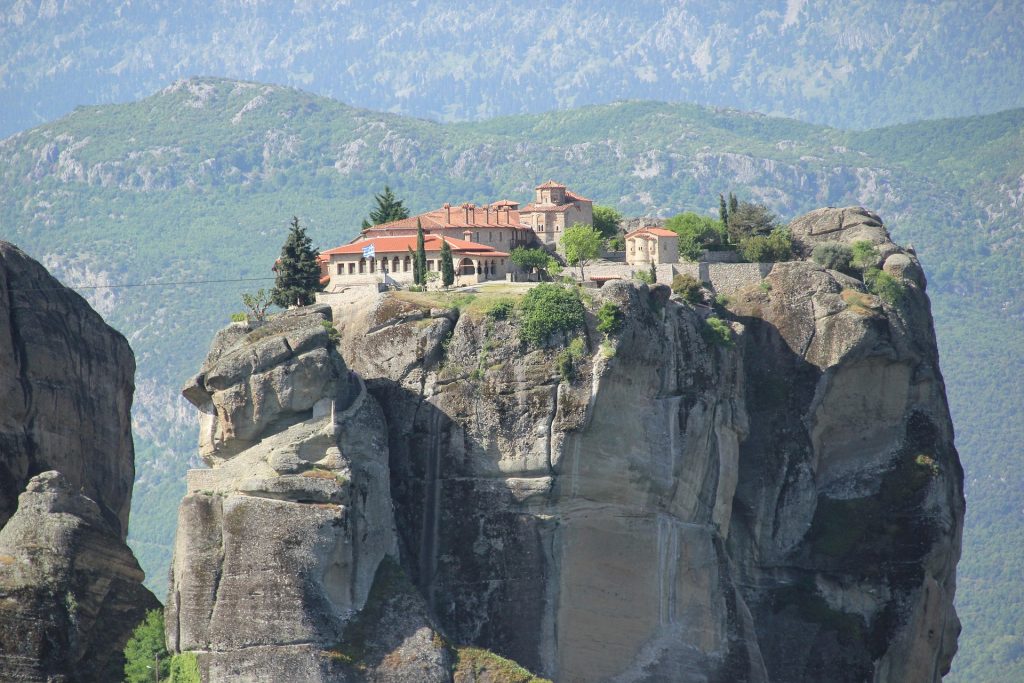 Historic Meteora monastery sitting atop a towering rock formation with panoramic mountain views and stunning natural landscapes in Greece.