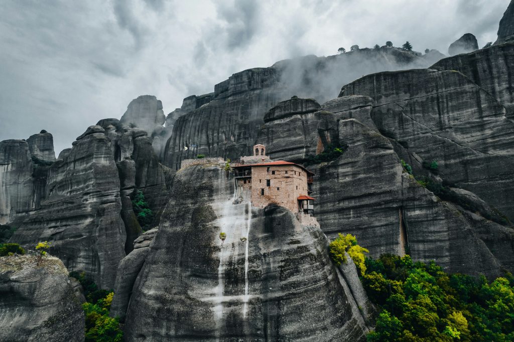 Monastery nestled among Meteora’s towering sandstone cliffs with misty scenery and breathtaking natural surroundings in Greece.