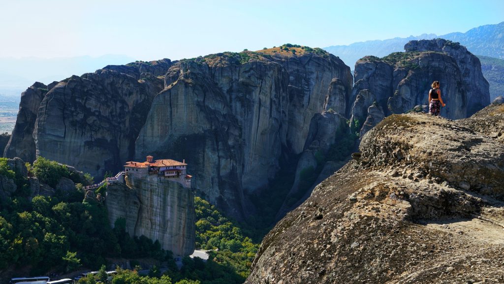 Hiker admiring the stunning Meteora landscape with monasteries perched on giant rock pillars and lush valleys below.