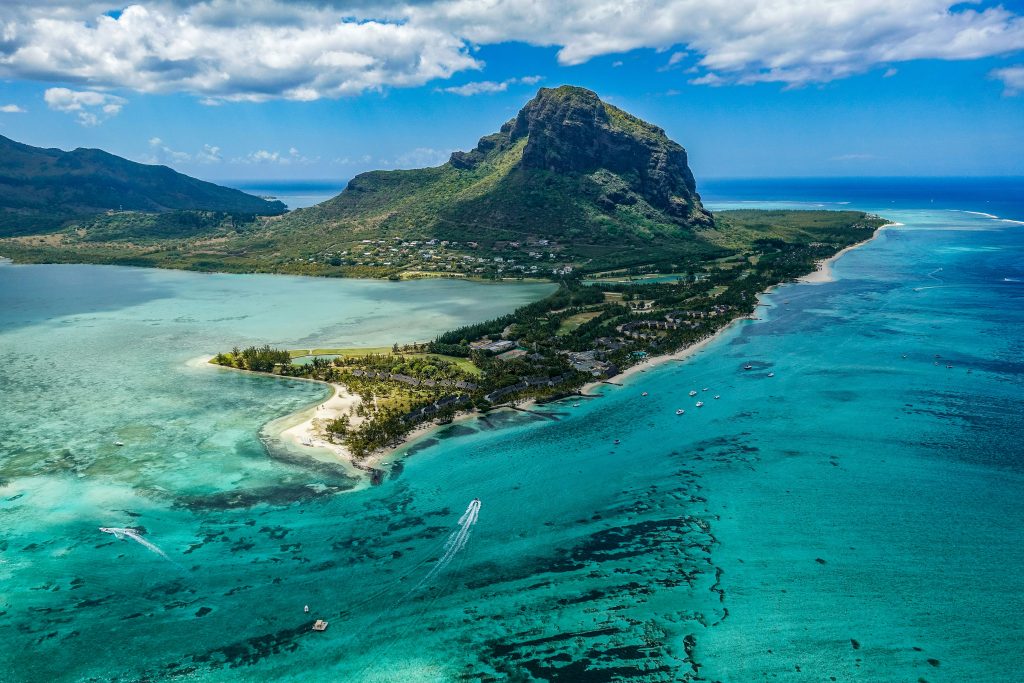 Aerial view of a tropical peninsula surrounded by turquoise lagoons, coral reefs, and a dramatic mountain rising above the coastline